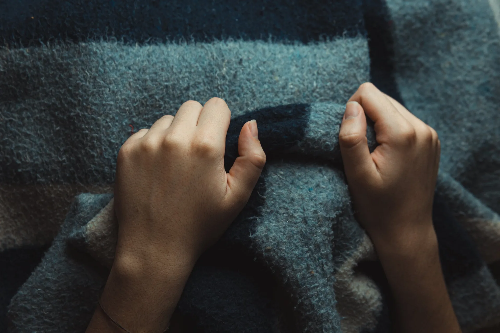 Two hands resting on a thick blue-grey wool blanket seen from above