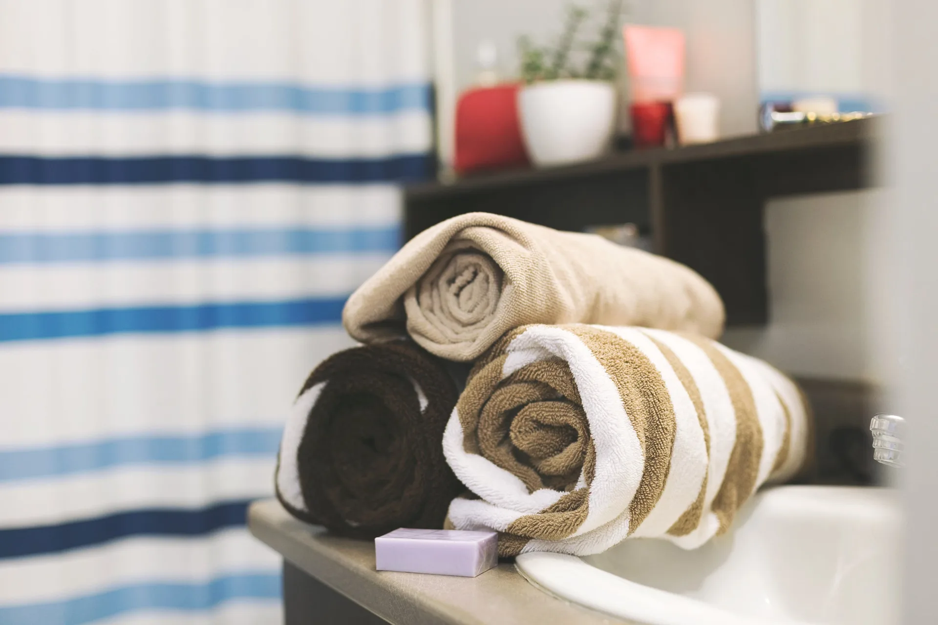 Rolled brown and striped bath towels and a small bar of soap on a bathroom counter