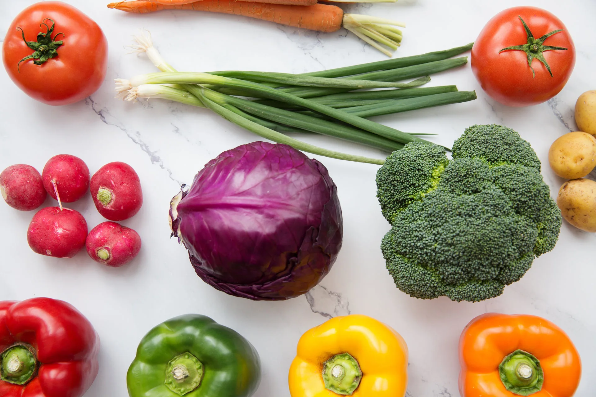Tomatoes, red cabbage, broccoli, radishes and colorful peppers arranged on a white marble surface