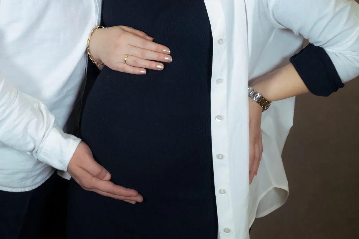 Two hands resting on a pregnant belly in a dark dress