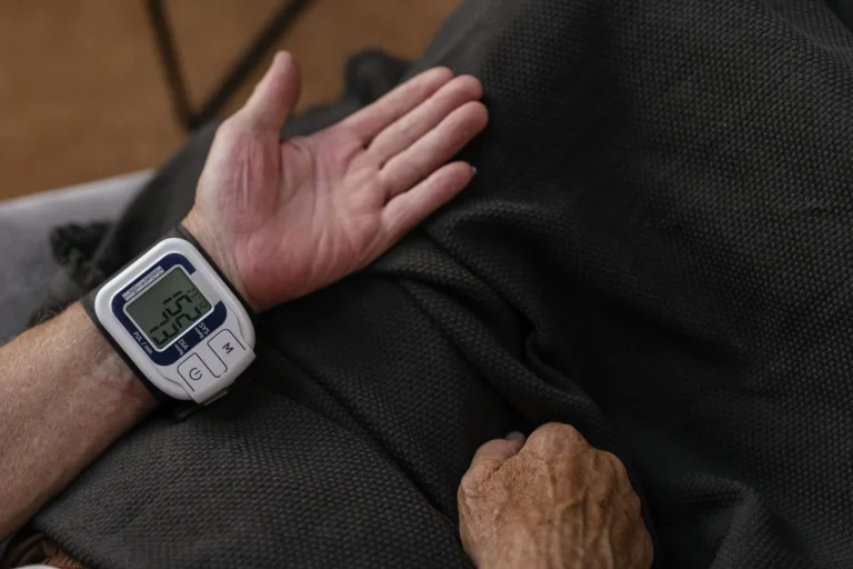 A person wearing a wrist blood pressure monitor resting one hand on their lap