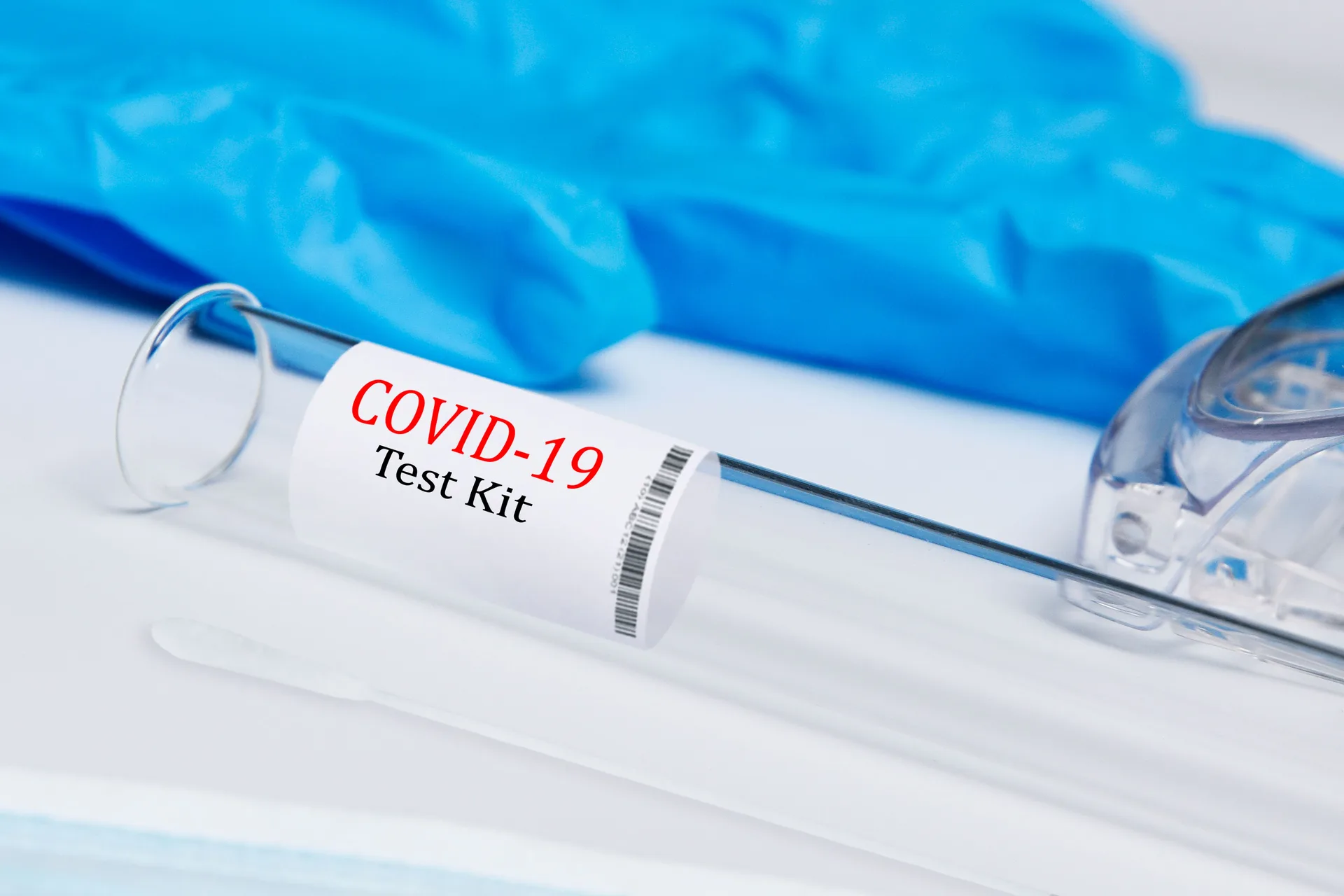 A test tube kit with a swab beside blue gloves and safety glasses on a white surface