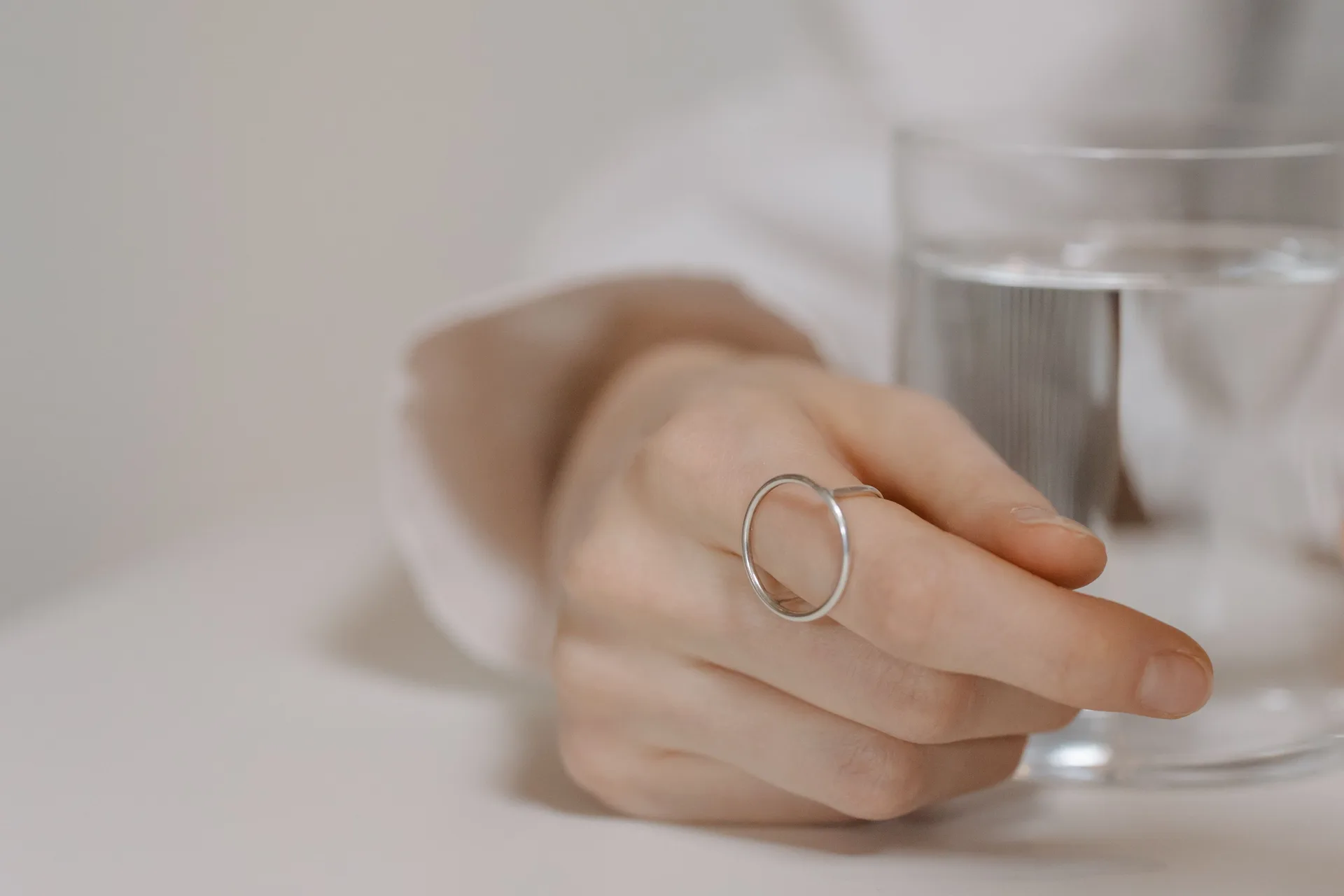 A hand with a silver ring resting beside a glass of water on a table