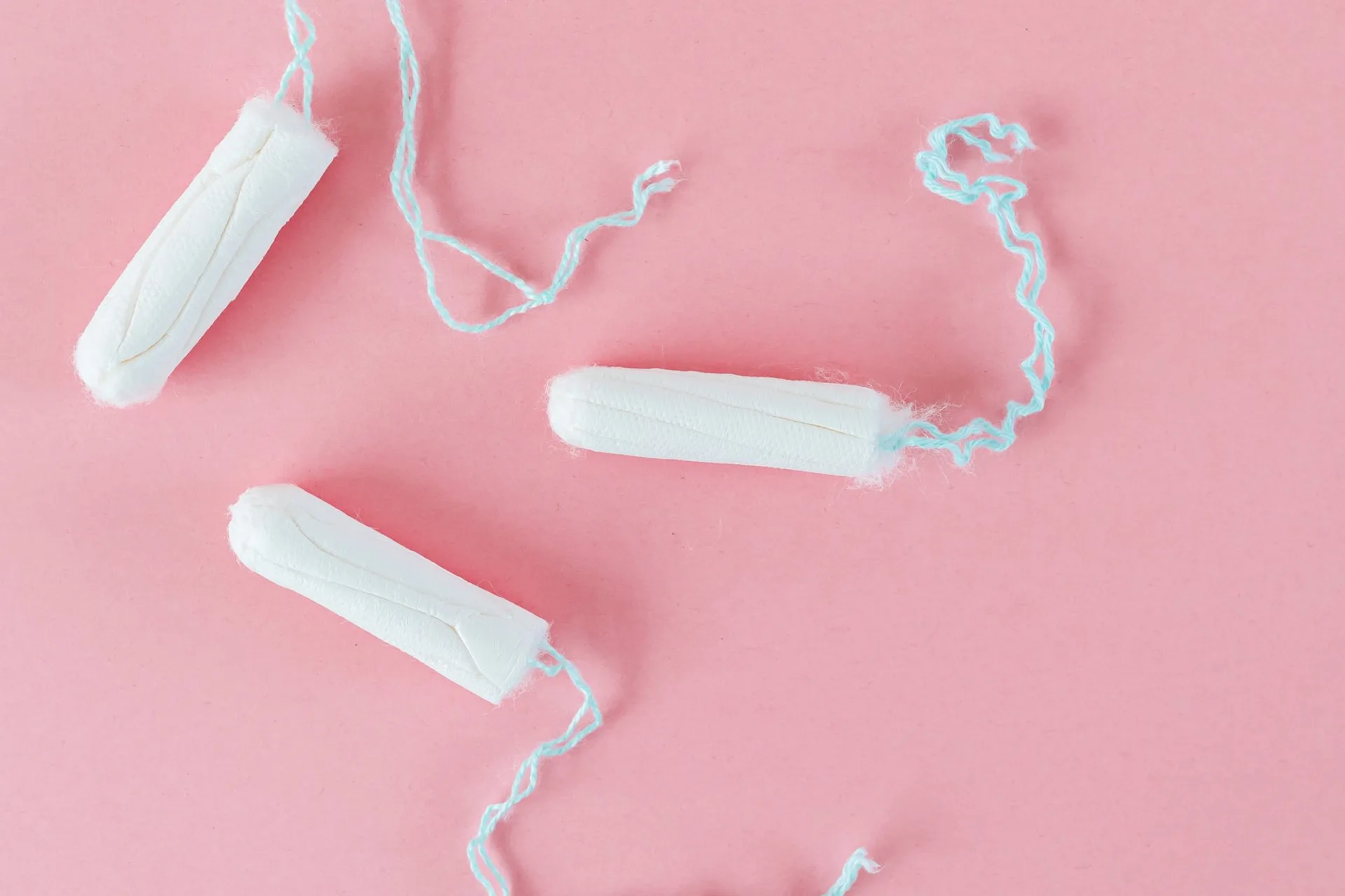 Three unbranded tampons with pale blue strings on a pink background