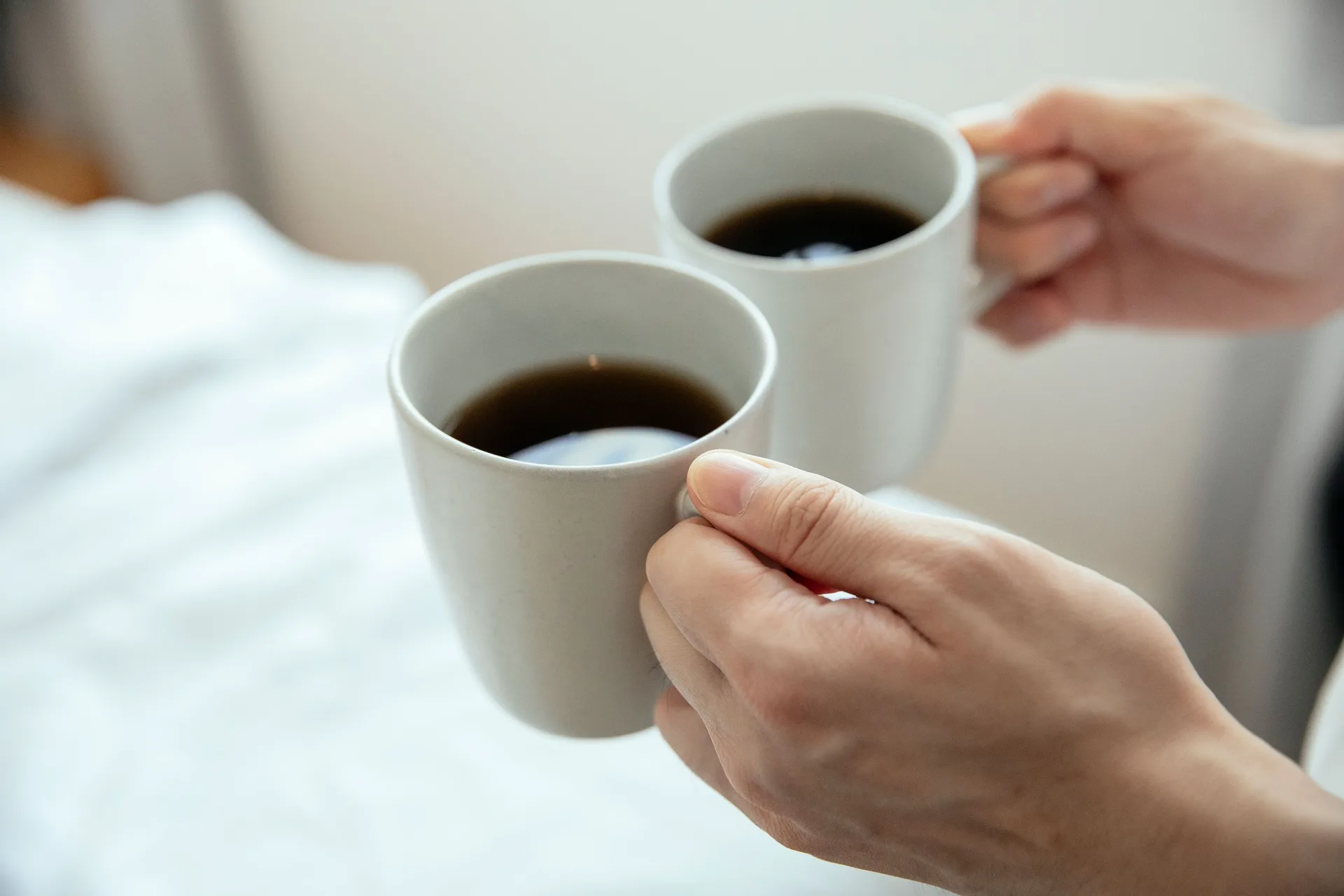 Two hands holding white mugs of black coffee toward each other
