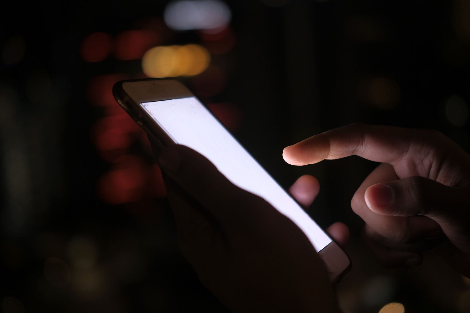 A hand scrolling a bright smartphone screen in a dark room