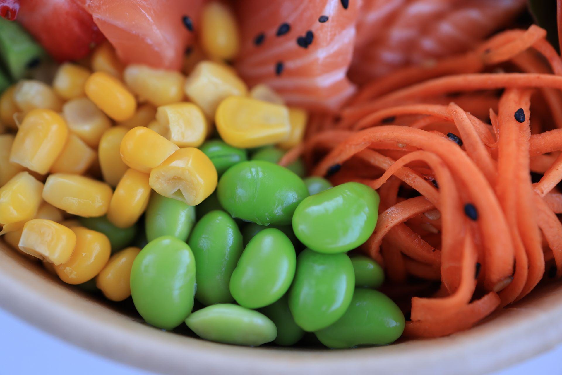 A close view of a salmon poke bowl with edamame, corn and shredded carrot