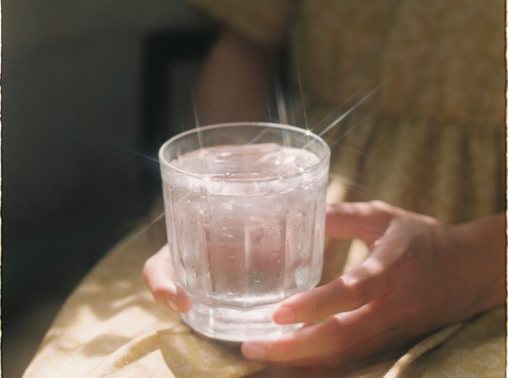 Hands holding a clear glass of water in sunlight.