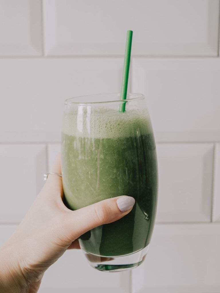 Hand holding a green smoothie, a hormone balancing recipe option for daily wellness