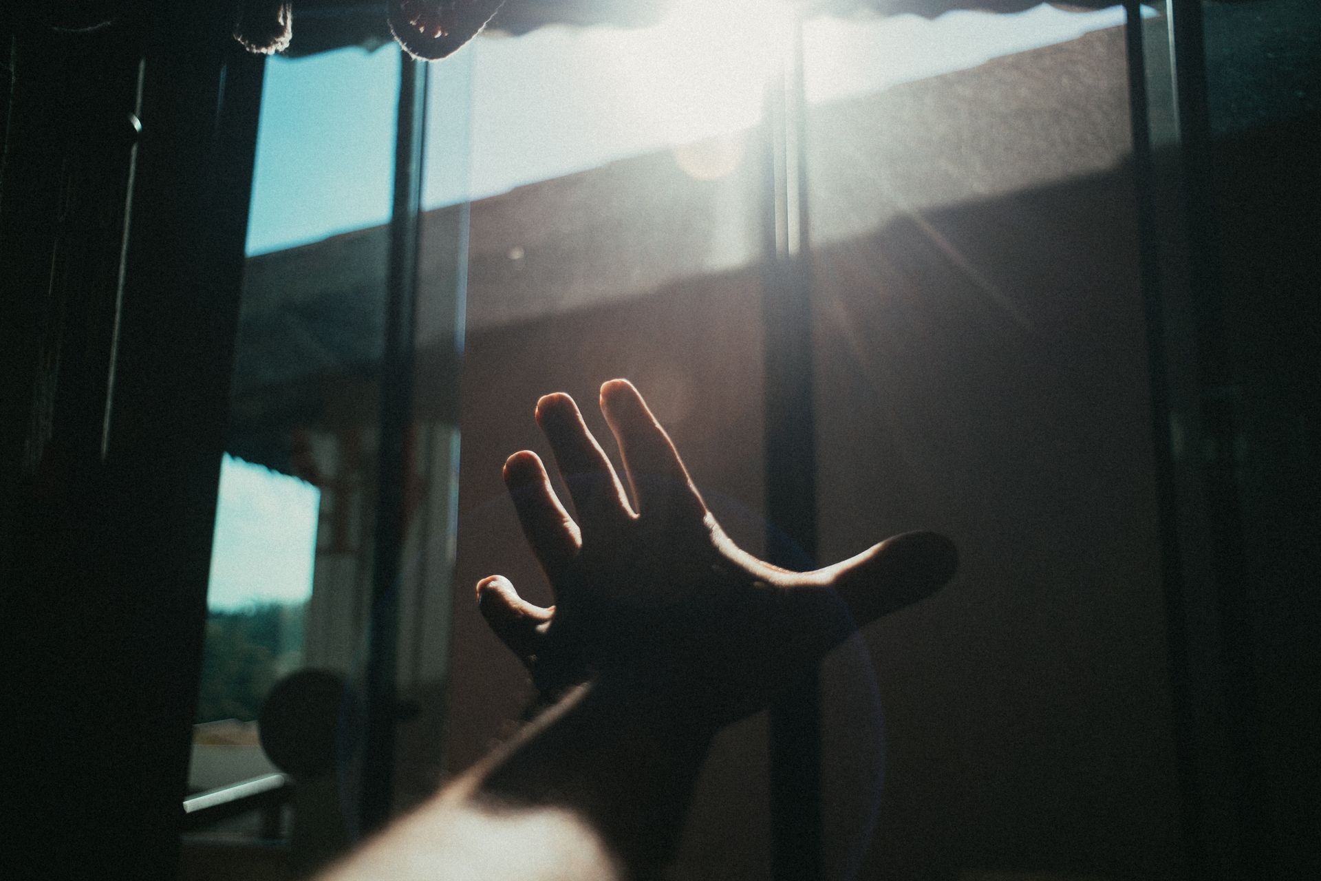 A hand reaching toward bright sunlight coming through a window