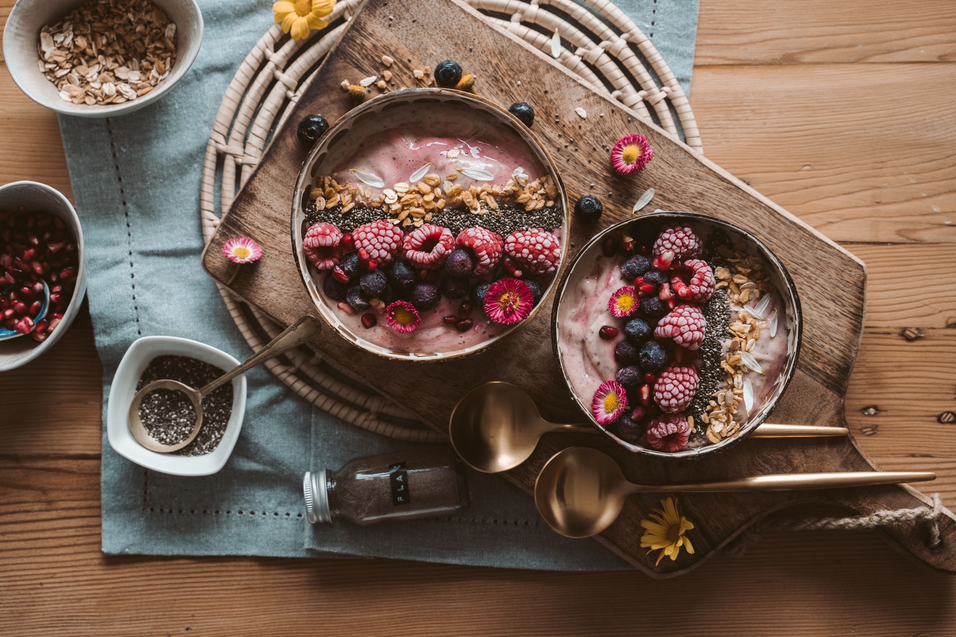 Two berry smoothie bowls topped with berries and granola on a wooden table