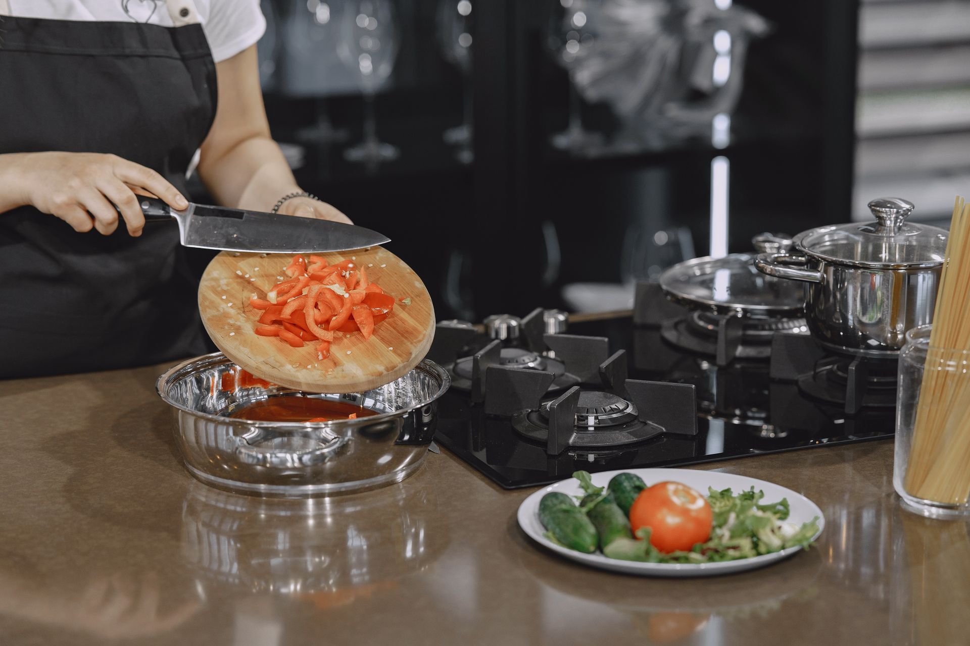 Hands sliding chopped red peppers from a cutting board into a cooking pot.