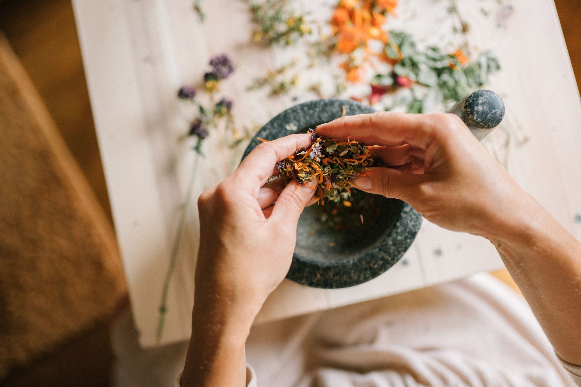 Hands crushing dried herbs and petals in a stone mortar