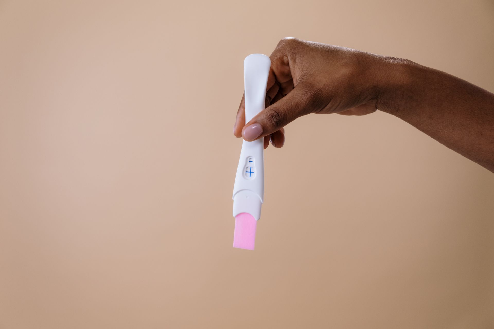 A hand holding a plain pregnancy test against a beige background.