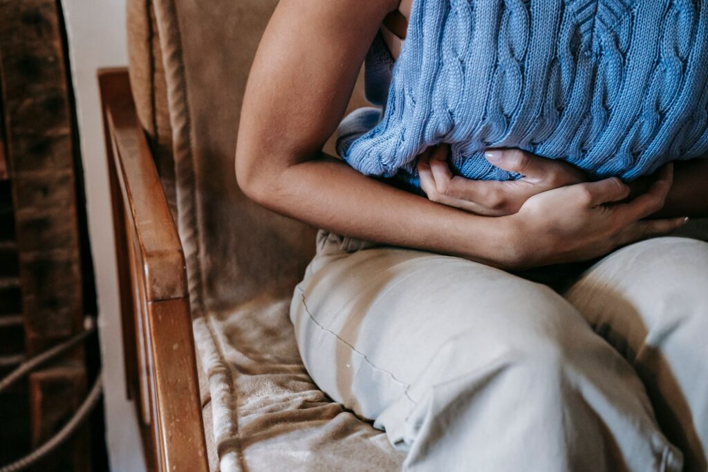 Woman sitting at home holding her stomach in pain from extreme PMS symptoms