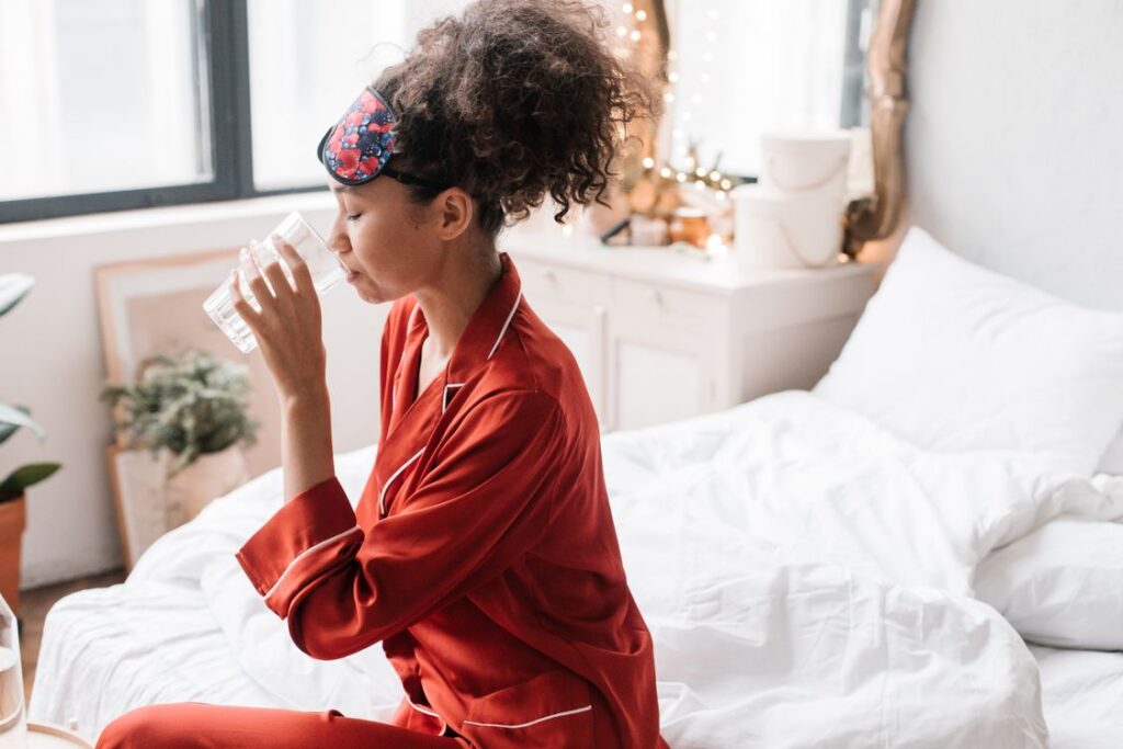 Woman in her bedroom drinking a glass of water as part of a daily wellness routine that supports vaginal and gut health