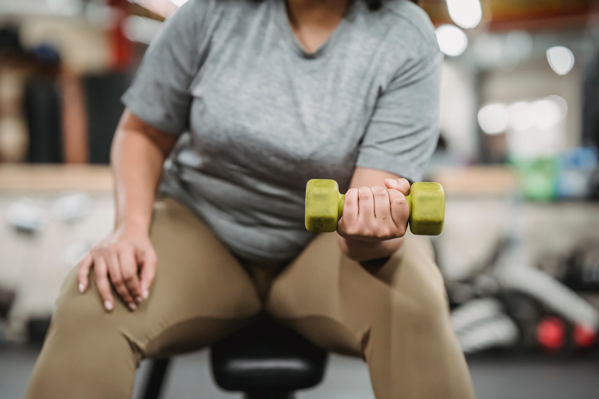 A seated person in activewear lifting a small dumbbell, shown without a face
