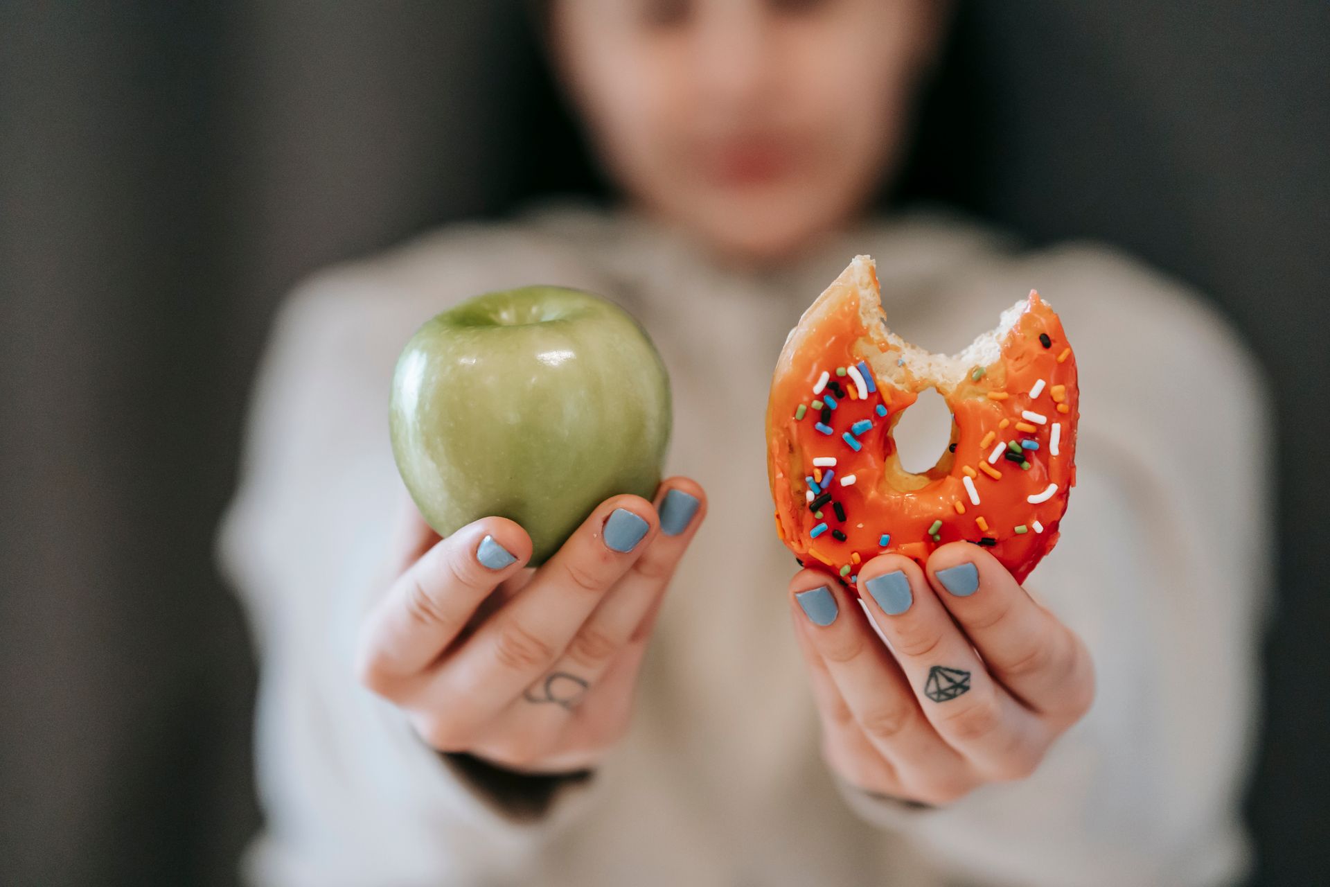 Hands holding a green apple in one hand and a bitten sprinkle doughnut in the other