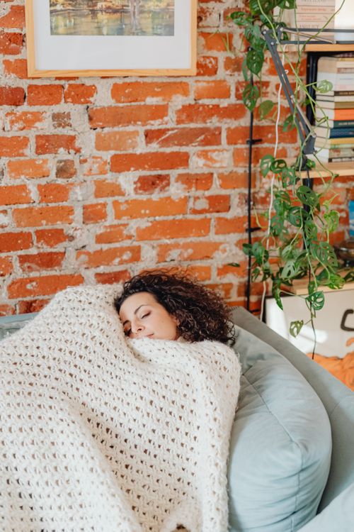 A woman rests wrapped in a cozy knitted blanket, reflecting the quiet exhaustion of undiagnosed iron deficiency