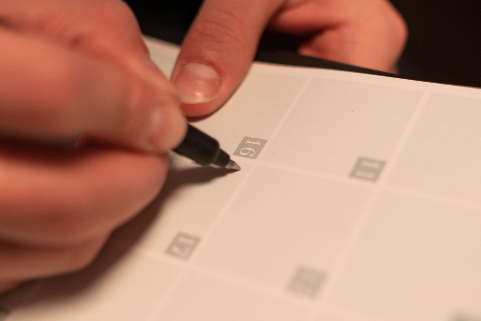 Hands marking a date on a paper calendar with a pen.