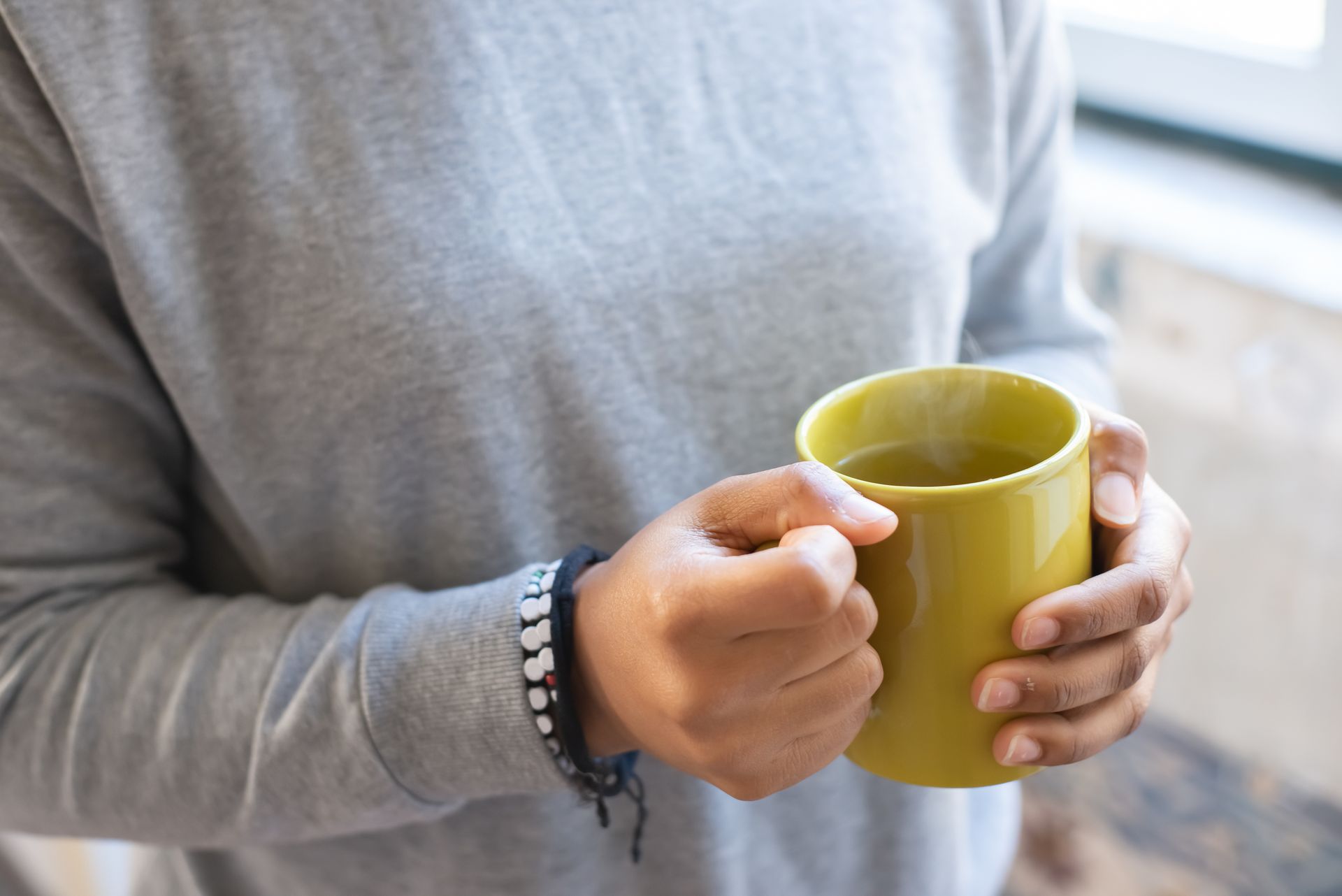 Hands holding a yellow mug of hot tea