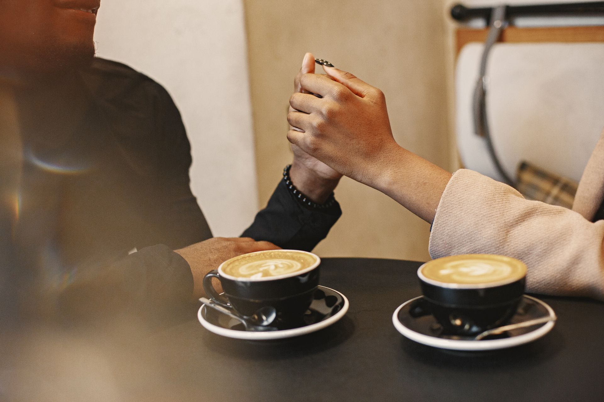 Two people holding hands across a café table beside two cups of coffee
