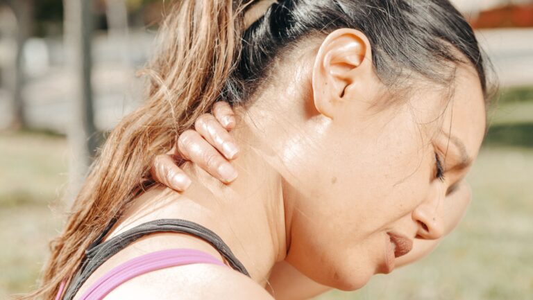 Close-up of a woman holding her neck in pain, illustrating the chronic pain and fatigue of fibromyalgia