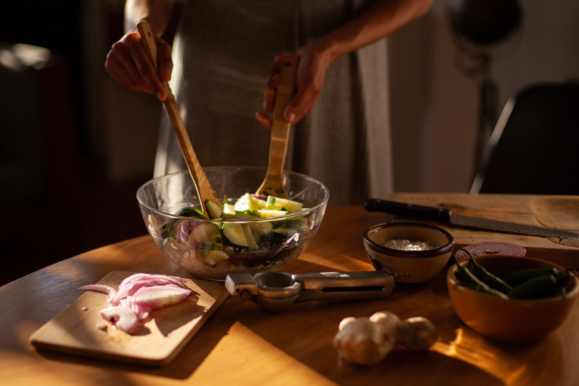 Hands tossing a vegetable salad in a glass bowl on a wooden table