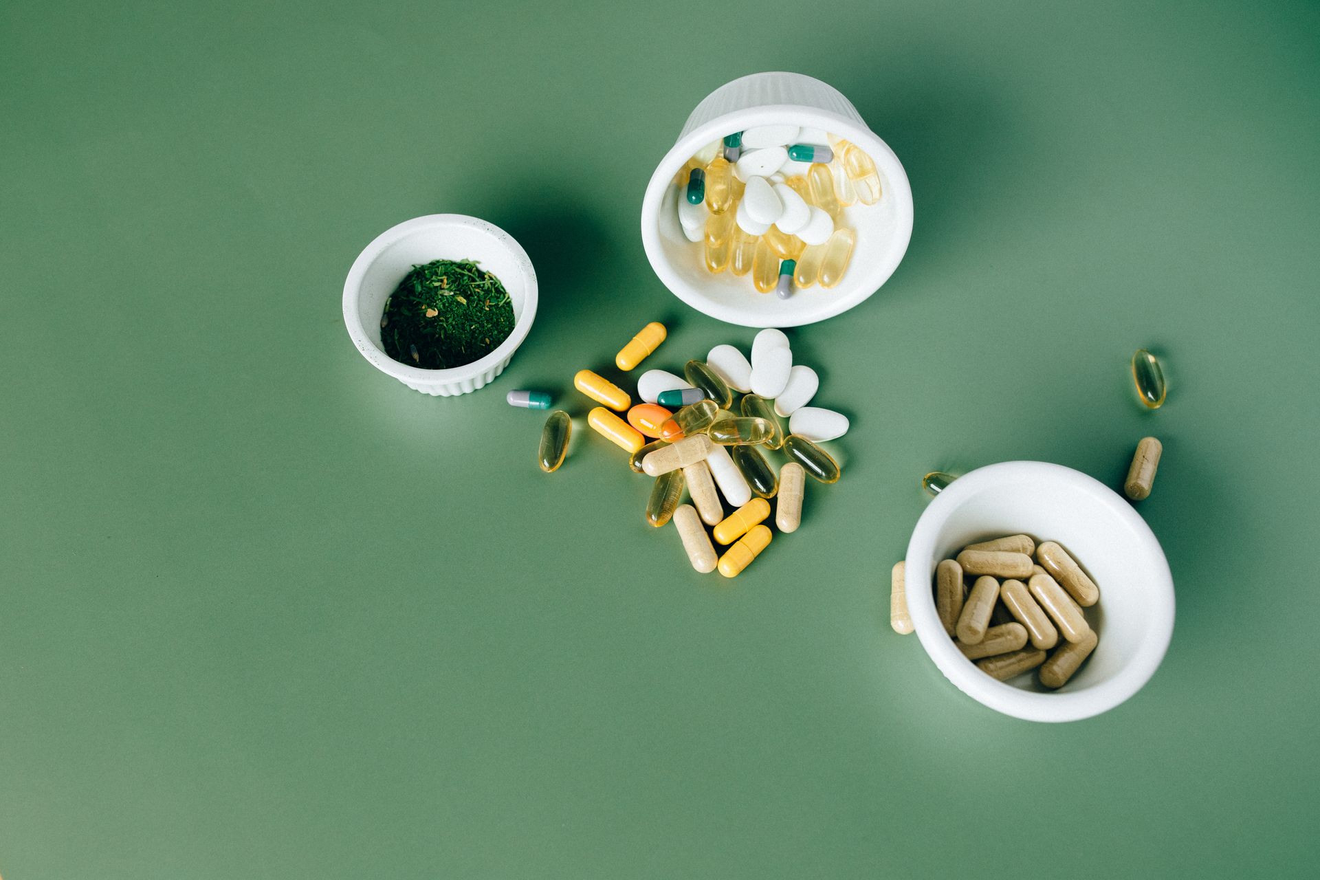 Capsules and tablets in small white bowls on a green surface