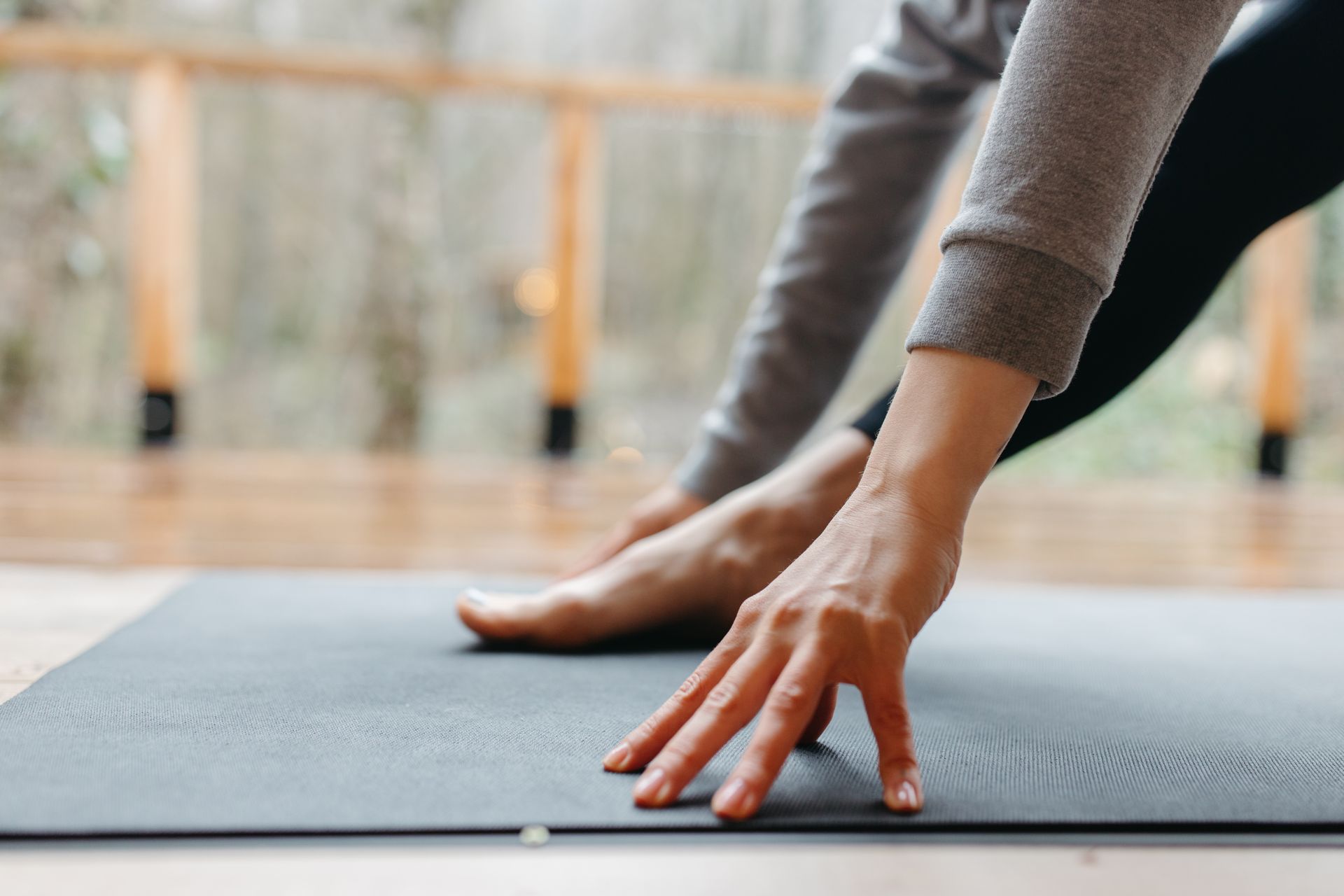 Hands and one foot resting on a dark yoga mat during a gentle stretch
