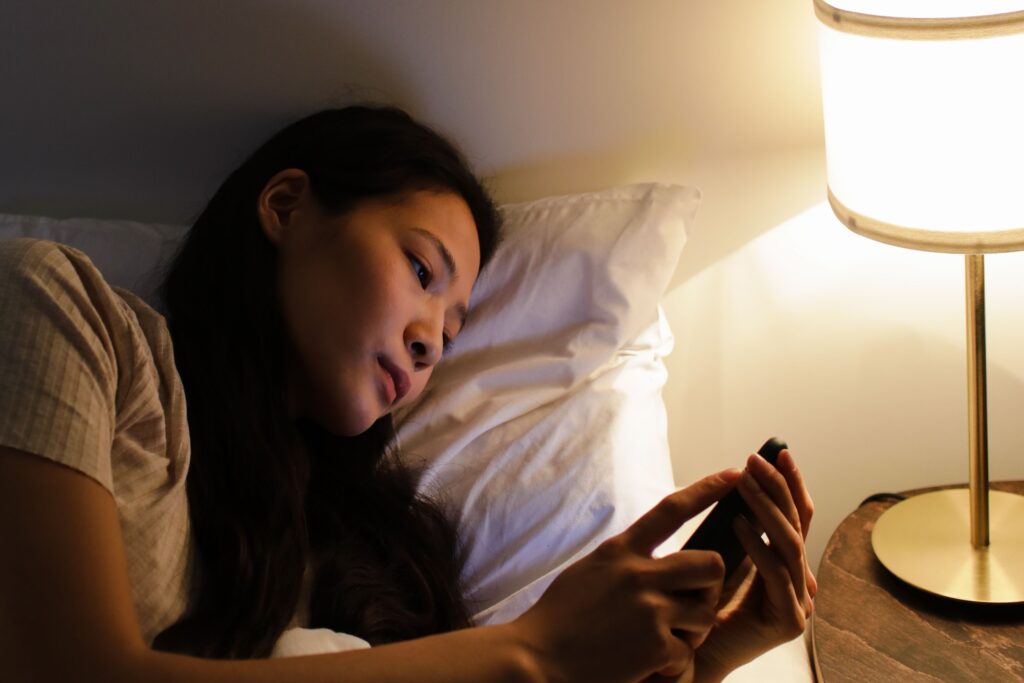 Woman lying awake in bed at night using her phone, unable to sleep