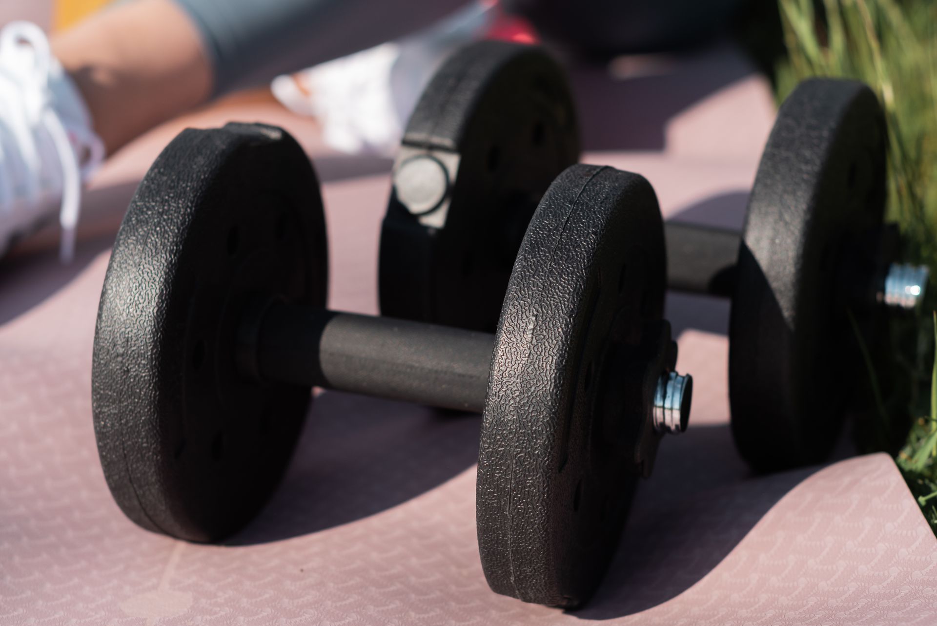 Black dumbbells on a pink exercise mat outdoors