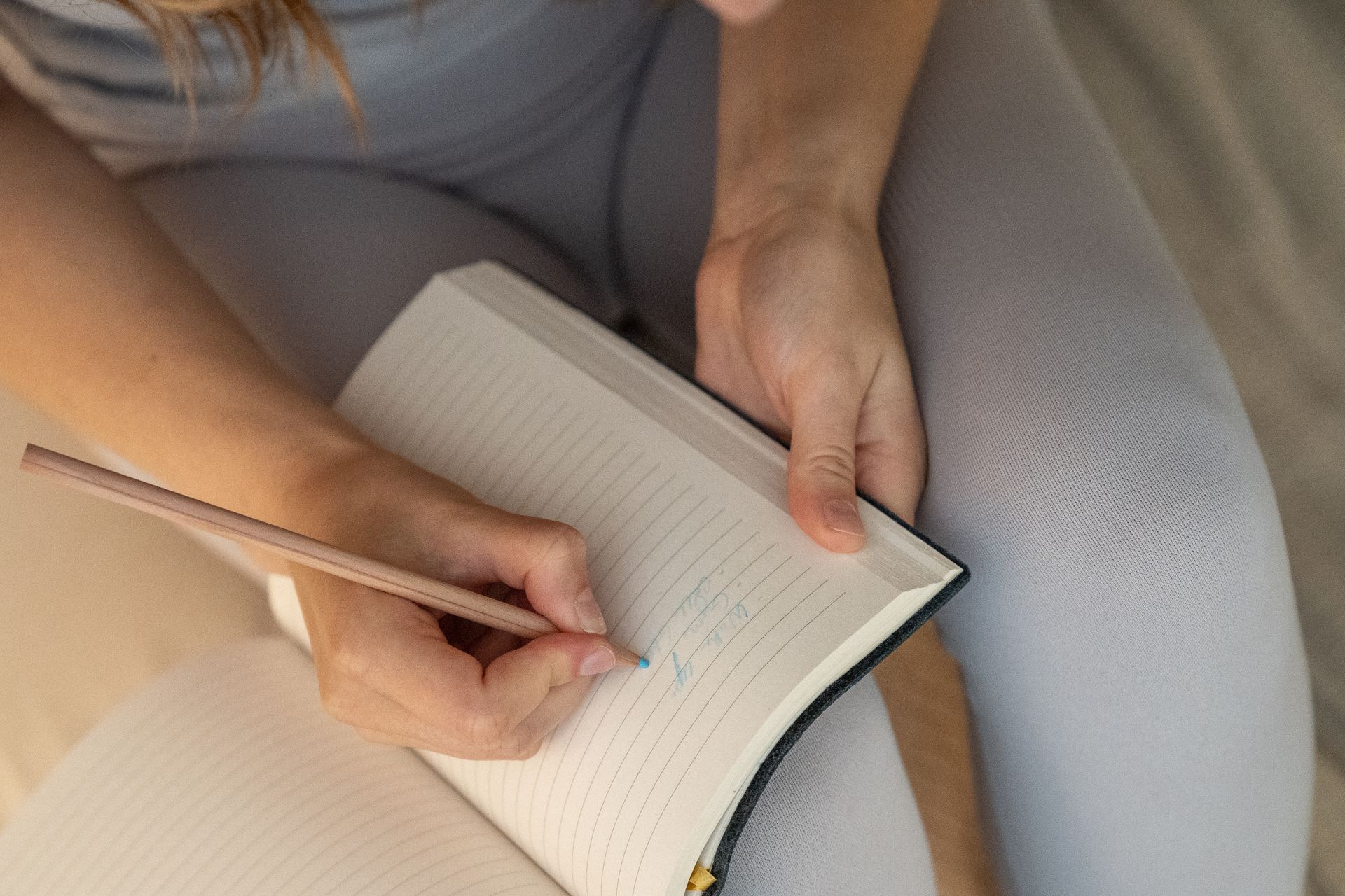 Hands writing in an open lined notebook with a pencil
