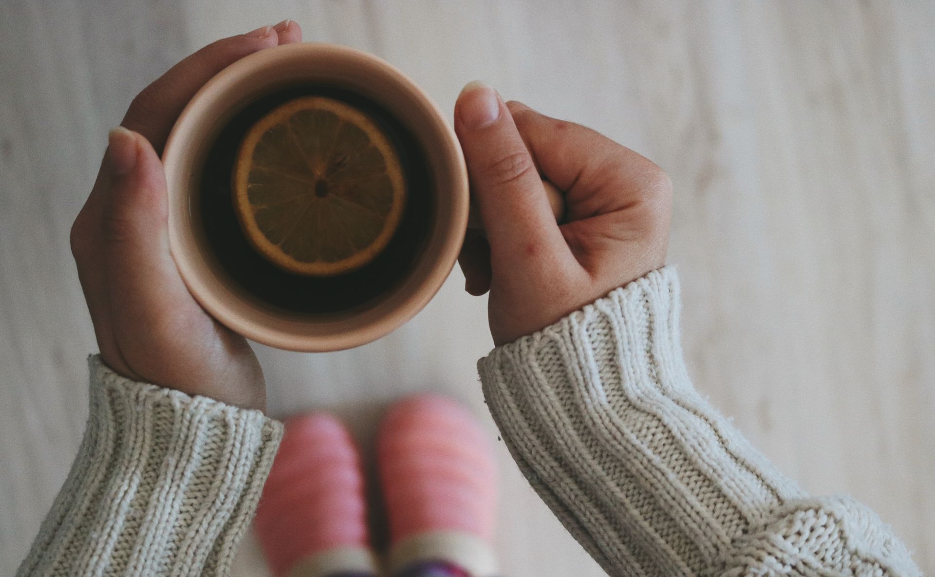 Two hands holding a cup of lemon tea, seen from above