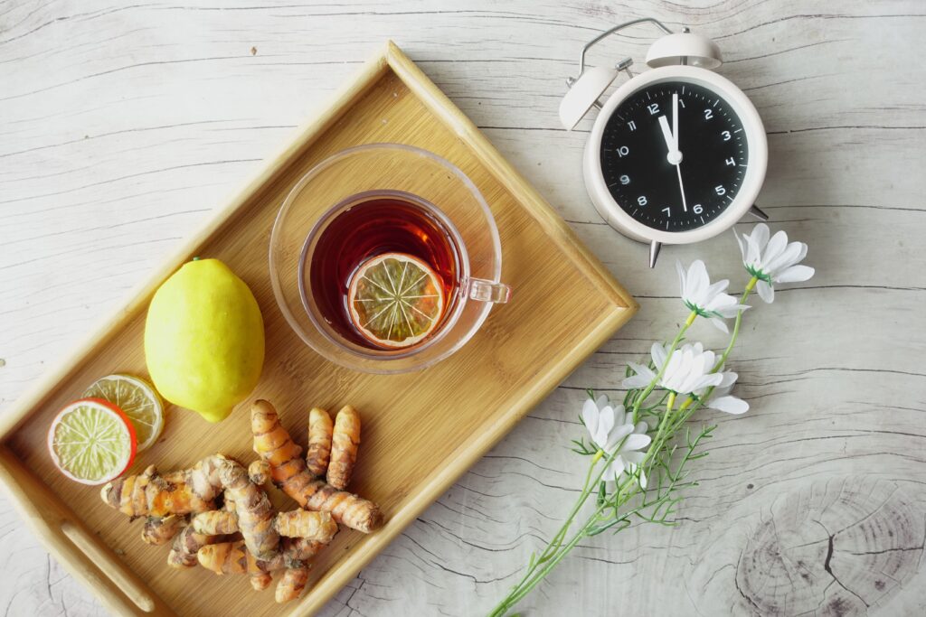 Herbal tea in a glass cup with fresh lemon, turmeric root, and flowers on a wooden tray, a natural approach to supporting hormone balance