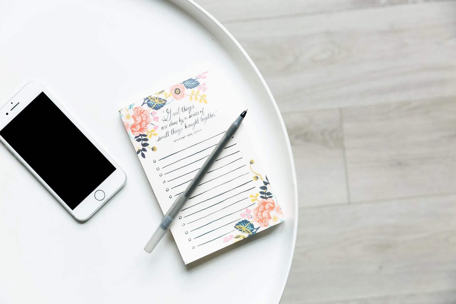 A phone and a notepad with a pen on a round white table