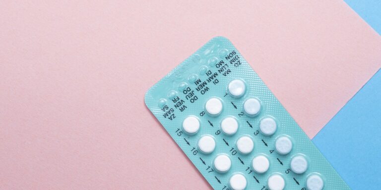 Teal blister pack of oral contraceptive pills on a pink and blue paper background