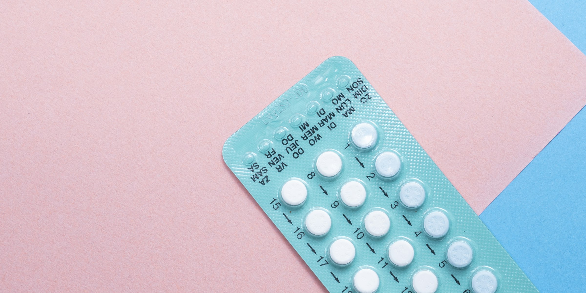 Teal blister pack of oral contraceptive pills on a pink and blue paper background