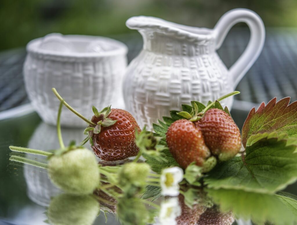 White ceramic pitcher of fresh strawberry-infused water on a bright, sunlit table
