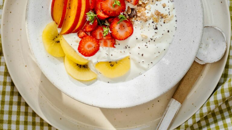 Bowl of plain yogurt topped with strawberries, kiwi, nectarine and granola