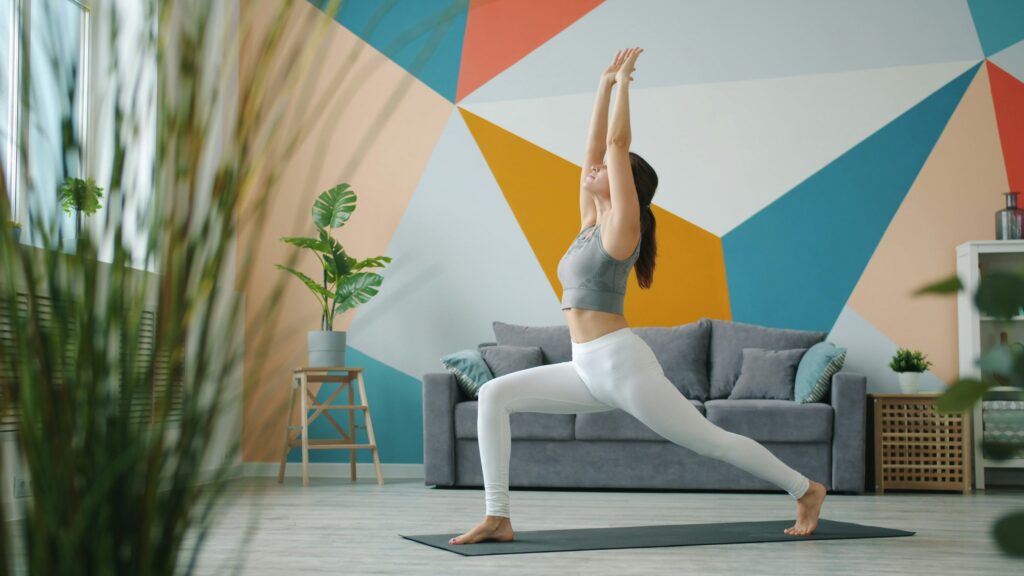Woman practicing gentle yoga stretches on a mat in a warm, sunlit living room
