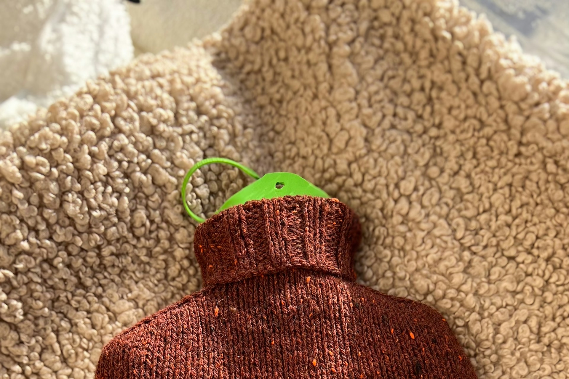 A knitted hot water bottle with a green stopper on a textured blanket.