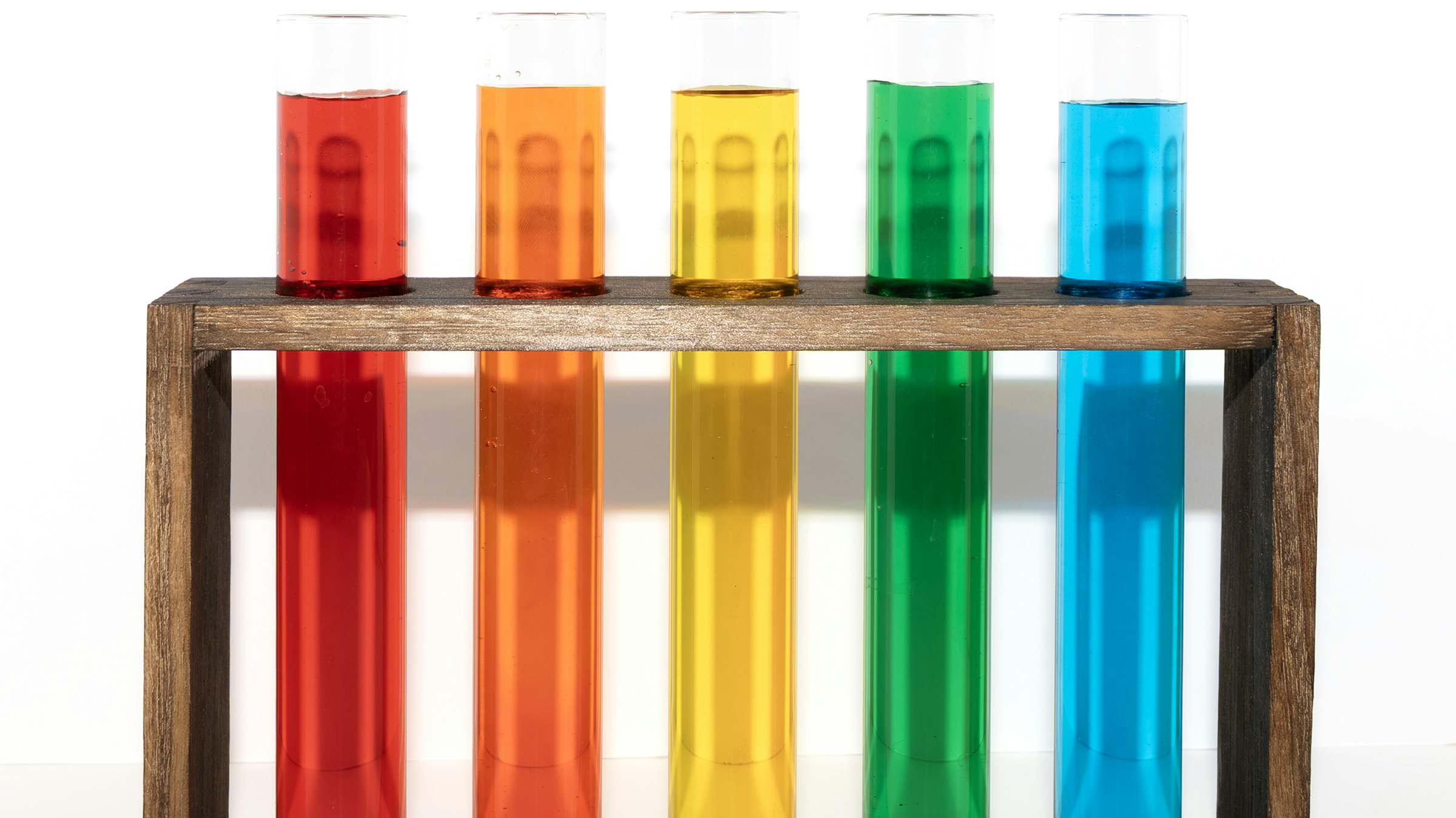 Five test tubes of red, orange, yellow, green and blue liquid in a wooden rack, like a pH color scale