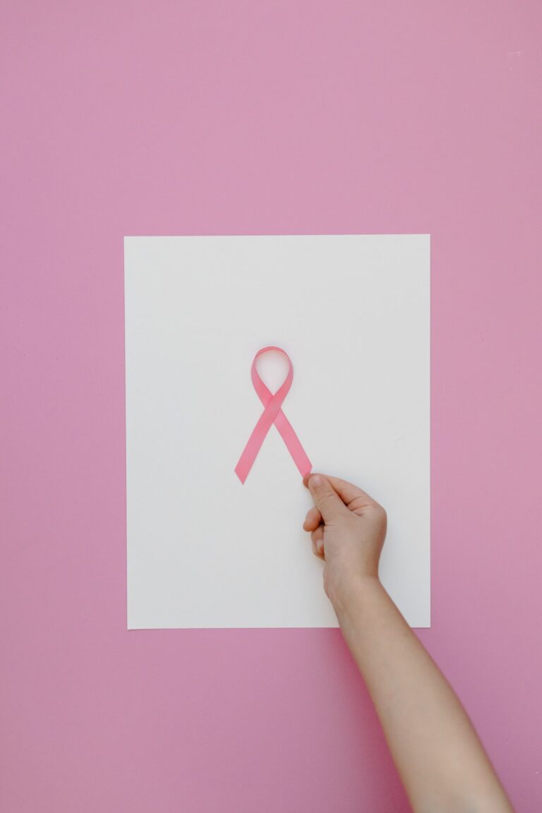 Hand holding a pink ribbon, the symbol of breast cancer awareness and support