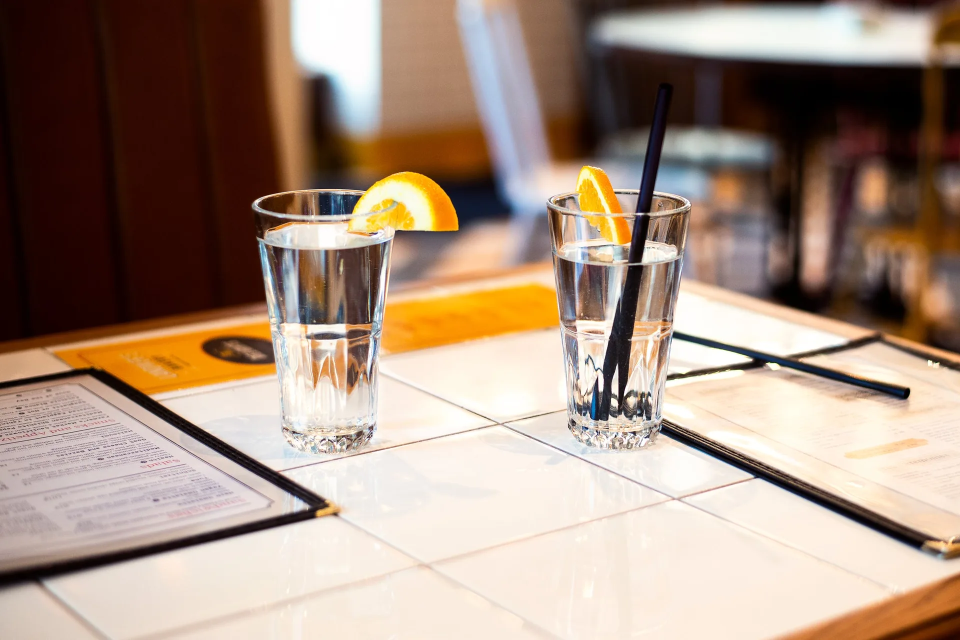 Two glasses of water, one with an orange slice, on a white tiled table