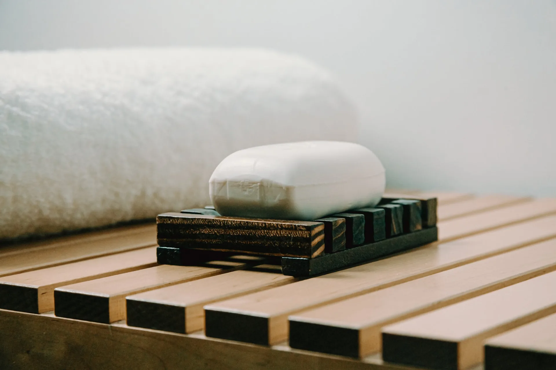 A bar of white soap on a wooden soap holder beside a folded white towel