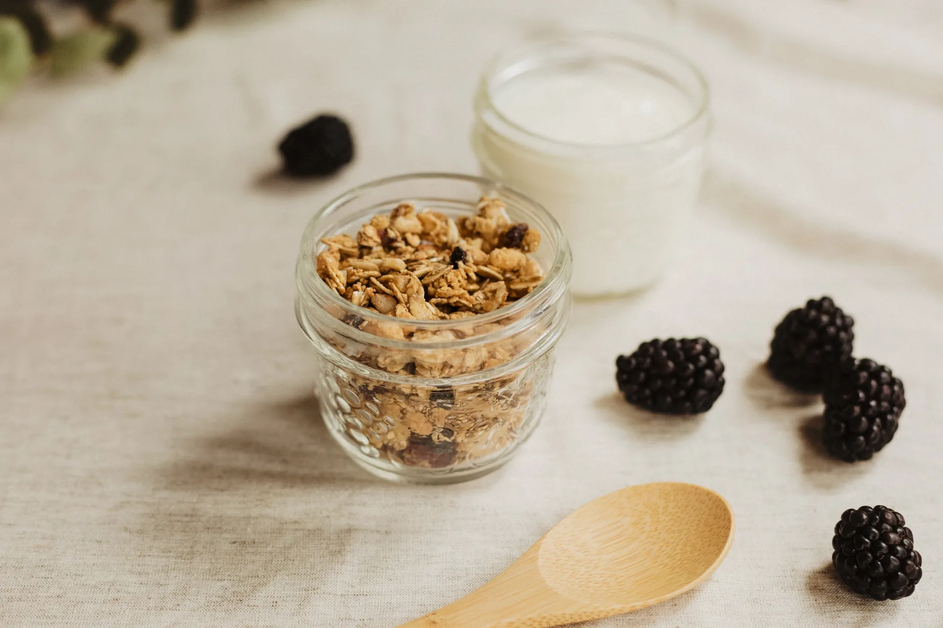 A jar of granola, a jar of yogurt and fresh blackberries on a linen cloth